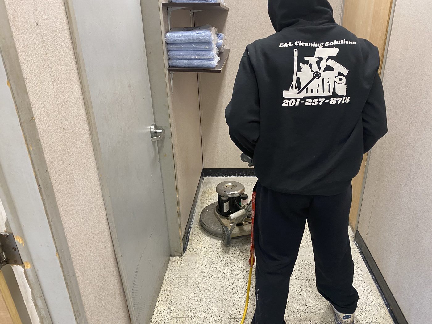 An E&L Cleaning Solutions crew member running a floor buffer, in a branded E&L jacket